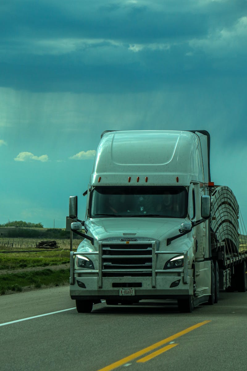 A white semi-truck travels on a highway under a cloudy, dramatic sky.
