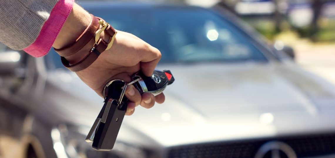 A close-up image of a hand holding car keys against the backdrop of a luxury car, outdoors.